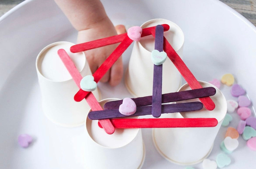 child balancing candy hearts on popsicle sticks and cups